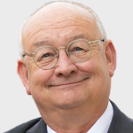 Smiling older man with glasses, a bald head, and wearing a suit and tie, facing the camera against a plain light background. EFESO Management Consultants